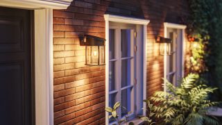 Modernus LED lauko sieninis šviestuvas apšviečia rustikinį medinį fasadą, pademonstruodamas energiją taupančius ir oro sąlygoms atsparius apšvietimo sprendimus šiuolaikinėms namų fasadams ir terasoms.